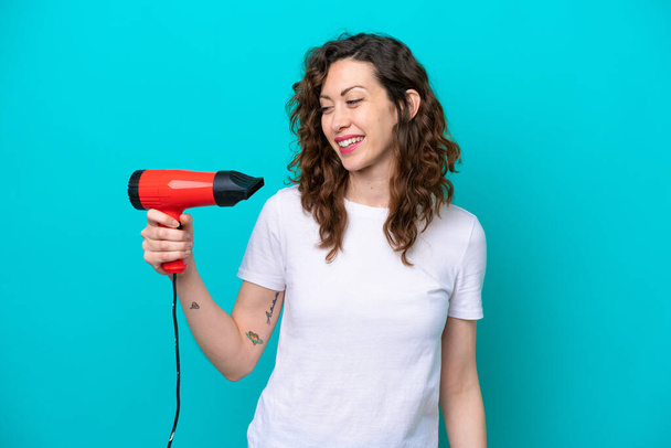 Young caucasian woman holding a hairdryer isolated on blue background with happy expression - Foto, imagen