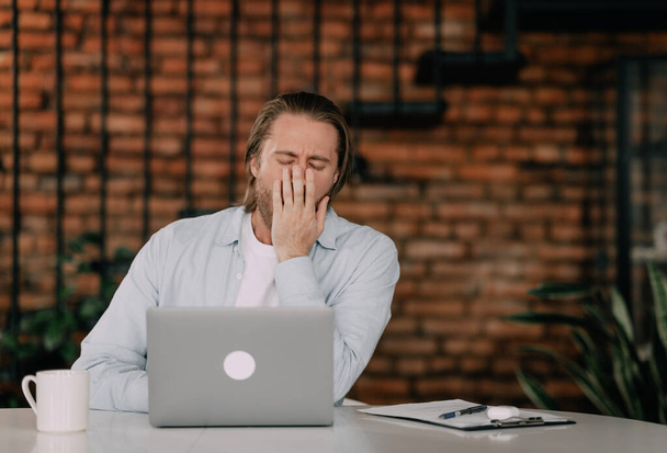 A man at his desk yawns while sitting at a computer. sleep deprivation concept. - Foto, immagini