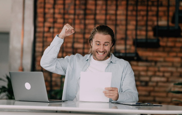Overjoyed employee shows happines ove clenching fists looking in some documents or reports. Successful young entepreneur. - Fotoğraf, Görsel