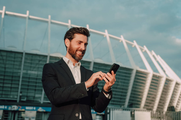 Successful businessman in a suit with a phone in his hands in a metropolis. Uses a business app and smiles. - Photo, Image