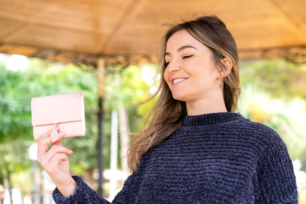 Giovane bella donna rumena in possesso di un portafoglio all'aperto con espressione felice - Foto, immagini