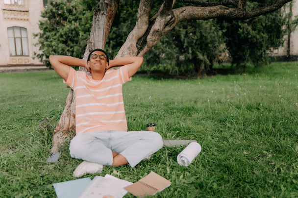 General scene of a campus life. Focus on african American student with glasses putting down his books and relaxing with his eyes closed. - Zdjęcie, obraz