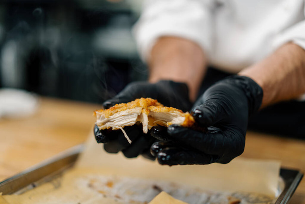 a chef in professional kitchen tears apart baked pieces of chicken fillet in breadcrumbs with his hands - Fotoğraf, Görsel