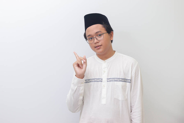 Retrato de un joven musulmán asiático mostrando producto y señalando con la mano y el dedo. Imagen aislada sobre fondo blanco - Foto, imagen