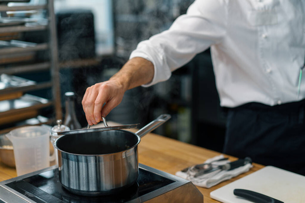 профессиональная кухня шеф-повар поднимает крышку горшка и проверяет готовность блюдо приготовления - Фото, изображение