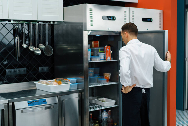 professional kitchen chef looks into fridge and chooses ingredients for cooking food concept - Foto, Imagen