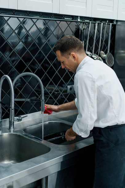 χαρούμενη επαγγελματίας σεφ στην κουζίνα πλύσιμο βρώμικα πιάτα στο νεροχύτη μετά το μαγείρεμα έννοια των τροφίμων - Φωτογραφία, εικόνα