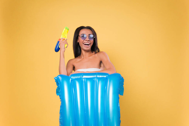 funny Young African American woman on a yellow background with an air mattress and a water gun. beach holiday and vacation concept - Zdjęcie, obraz