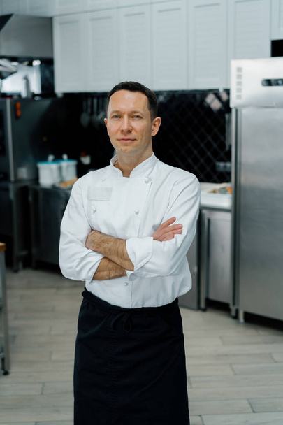 cozinha profissional sorrindo e satisfeito chef casaco branco de pé com braços cruzados retrato - Foto, Imagem