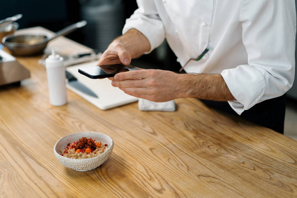 profesjonalna kuchnia kucharz robi zdjęcie świeżo przygotowanej owsianki z karmelizowanymi owocami na śniadaniu smartfona - Zdjęcie, obraz