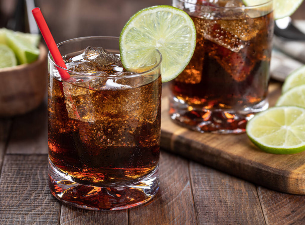Rum and cola cocktail with lime slice on rustic wooden table.  Closeup - Foto, afbeelding
