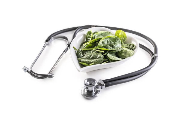 Symbol of healthy heart with stetoscope and heart-shaped bowl full of baby spinach leaves on an isolated white background. - Photo, image