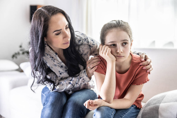 Offended young daughter sulks on a couch while her mother tries to talk to her. - Photo, image