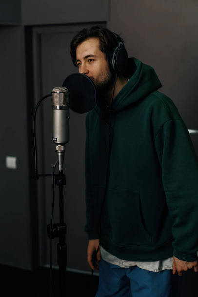 τραγουδιστής με ακουστικά και μικρόφωνο ηχογραφεί συναισθηματικά ένα νέο τραγούδι σε επαγγελματικό στούντιο ηχογράφησης - Φωτογραφία, εικόνα