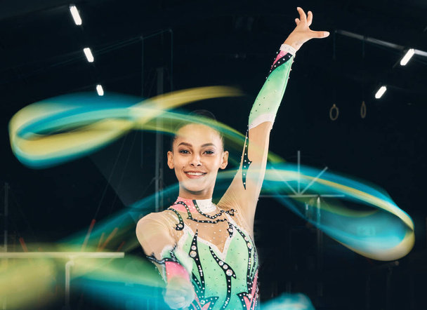 Ribbon gymnastics, happy woman and portrait of motion, dancing performance and competition in dark arena. Female dancer, rhythmic movement and solo routine of creative talent, sports concert or smile. - Foto, Imagen