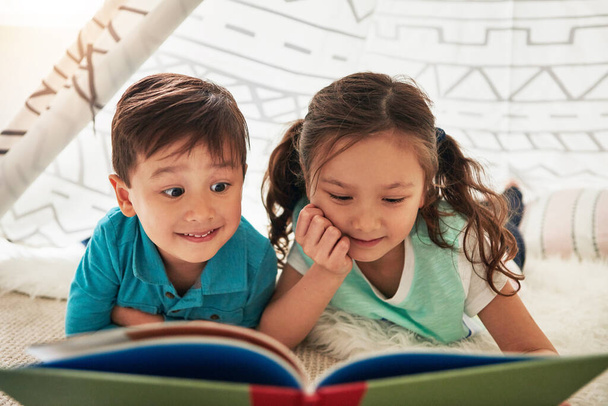 Αφήνουν τη φαντασία και την περιέργειά τους να ταξιδεύουν μέσα από βιβλία. δύο αξιολάτρευτα μικρά αδέλφια που διαβάζουν ένα βιβλίο μαζί στο σπίτι - Φωτογραφία, εικόνα