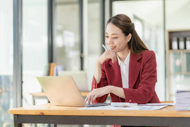 Улыбающаяся азиатская бизнесвумен, работающая за планшетным компьютером за своим столом в ярком современном офисе - Фото, изображение