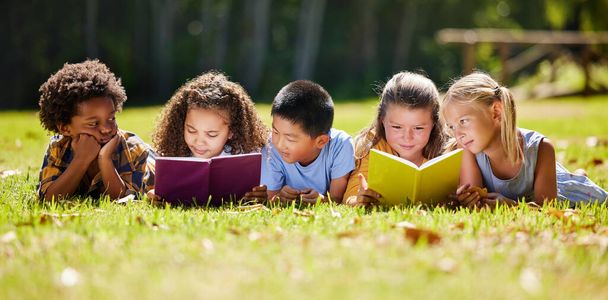 Children, books and lying in park with friends, learning or diversity for reading at school playground. Kids, education or study with support, mockup space or solidarity at multicultural kindergarten. - Φωτογραφία, εικόνα