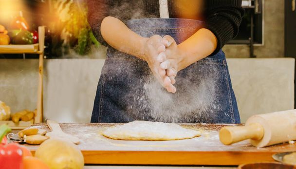 Ruce kuchařky připravující pizzu, proces míchání pšeničné mouky tak, aby byla rovnoměrně rozložena na těsto pizzy na stolek s válečky, aby ji změkčila v kuchyni v restauraci. - Fotografie, Obrázek