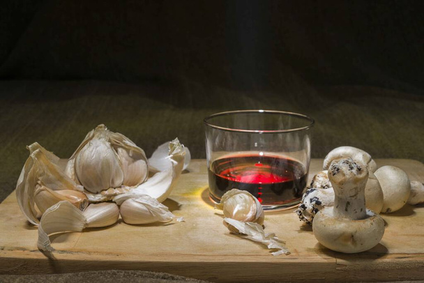 Натюрморт з келихом вина, часнику та грибів на дерев'яній дошці
 - Фото, зображення