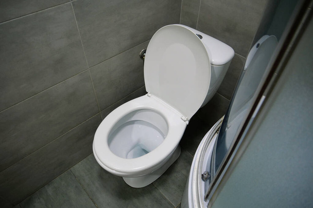 Інтер'єр туалетної кімнати з білим унітазом, душовою кабіною та сірою плиткою
 - Фото, зображення