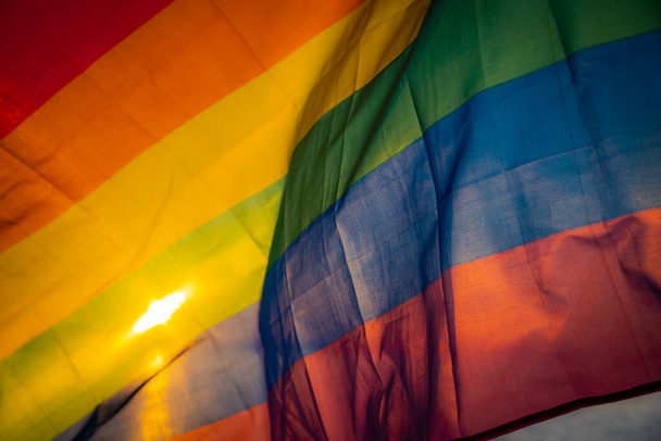 Flaga LGBT na tle zachodu słońca nad jeziorem. LGBT gejowska flaga dumy, lesbijki, geje, biseksualiści, transgenderowe ruchy społeczne. Koncepcja wolności szczęścia, miłość do pary jednopłciowej. Flaga machająca pod wiatr - Zdjęcie, obraz
