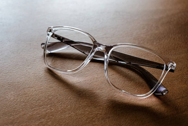 Glasses in a transparent frame on a wooden table, closeup. - 写真・画像
