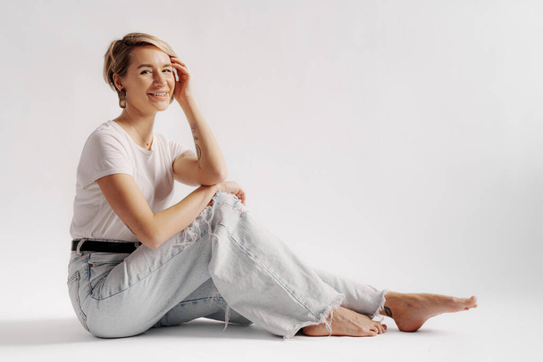 Full body of young barefoot female sitting on floor while relaxing against white background - Foto, Imagem