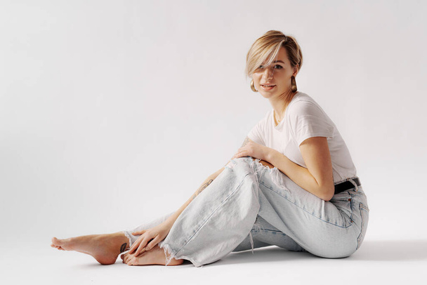 Full body of young barefoot female sitting on floor while relaxing against white background - Foto, Imagen