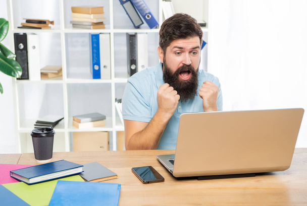 Excited businessman making fists looking in laptop at office desk, anticipation. - 写真・画像