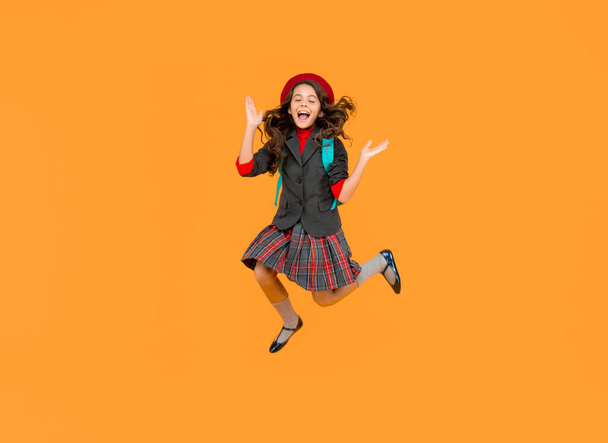 glad teen girl in uniform and beret with school bag running on yellow background, schoolgirl. - Fotografie, Obrázek