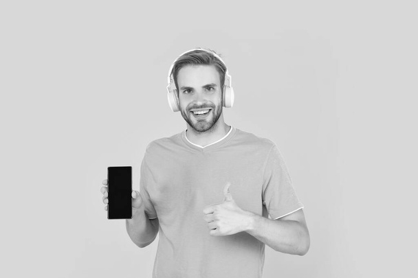 The best phone. Happy guy give thumbs up to mobile phone. Music smartphone. Listening to podcast or watching video. Use it to make you feel different. - Photo, Image