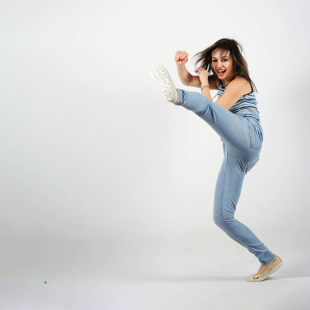 Young woman dancing hip-hop in the studio. White background, hands and left leg kicking in the air - Фото, зображення