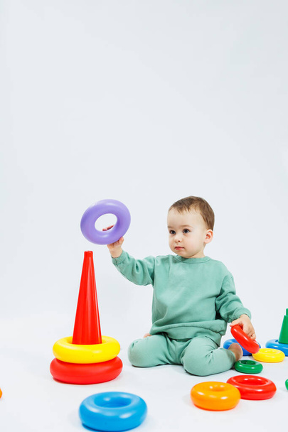 Little boy playing logic educational games with plastic pyramid isolated on white background. A happy child plays with an educational toy. The baby is one year and four months old - Photo, Image