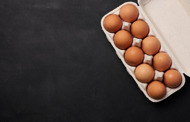 Syrové hnědé kuřecí vejce v papírové lepenkové nádobě na černém pozadí, horní pohled. Kopírovat prostor - Fotografie, Obrázek