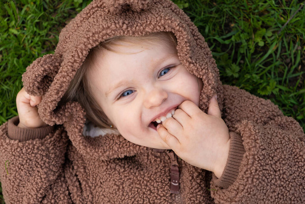 Ritratto di una bambina di un anno e mezzo sdraiata sull'erba e con le dita in bocca. - Foto, immagini