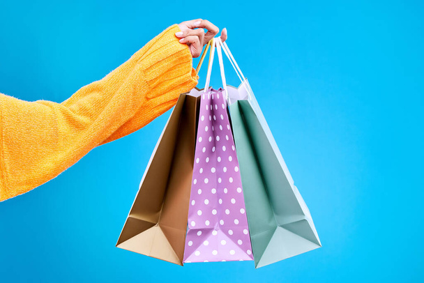 Woman, hands and shopping bags in studio of purchase, luxury accessories or sale against a blue background. Hand of female shopper holding gift bag, buy or presents of retail products on mockup. - Photo, image