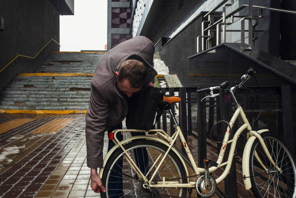 Egy öltönyös és kabátos üzletember egy esős napon, lovaglás előtt ellenőrzi a biciklije kerekeit. biztonsági ellenőrzés. - Fotó, kép