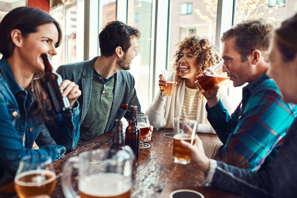 Η φιλία μας έφερε κοντά, η μπύρα μας κρατάει μαζί. νέοι που πίνουν μπύρες σε ένα μπαρ - Φωτογραφία, εικόνα