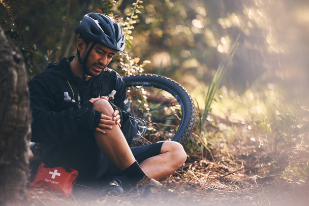 Man, cycling and outdoor with leg or knee injury in nature for sports, exercise or training on mountain bike. Athlete person with bicycle and first aid for fitness workout accident or fall in forest. - Photo, Image