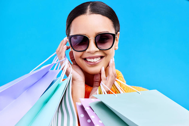 Shopping bags, studio and happy woman portrait with a smile and happiness from boutique sale. Sunglasses, customer and female model with store bag and sales choice in isolated blue background. - Fotoğraf, Görsel