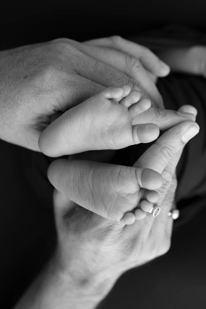 Black and white shade beautiful shape hands of mother, hold tiny newborn baby feet on black background with love, care, family safety and protection, child with premature birth concept or NICU care - Foto, afbeelding