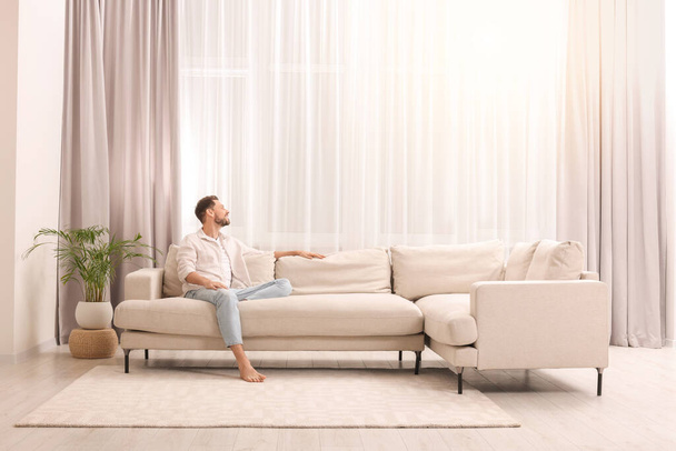 Happy man resting on sofa near window with beautiful curtains in living room - Foto, immagini