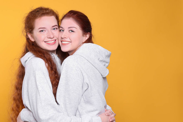 Portrait of beautiful young redhead sisters on orange background. Space for text - Фото, зображення
