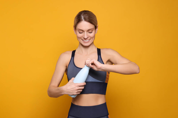 Sportswoman with thermo bottle on yellow background - Фото, зображення