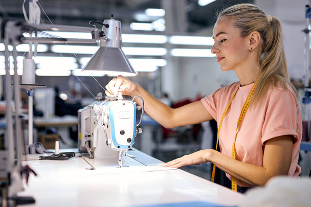 young woman sewing with professional machine at workshop,Clothing factory. female on sewing department, tailors studio, sewing school, clothing manufacturing, sewing industry - Zdjęcie, obraz