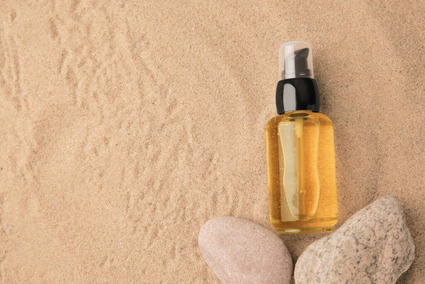 Bottle of serum and stones on sand, flat lay. Space for text - Foto, Imagen