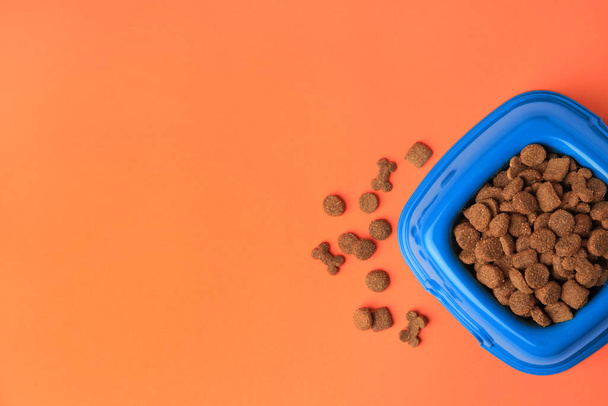 Dry pet food in feeding bowl on orange background, flat lay. Space for text - Photo, image