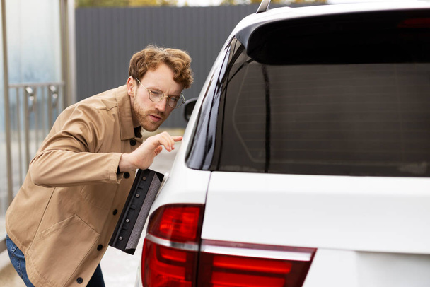 Jóképű férfi óvatosan törli az autót ablaktörlővel. Az önkiszolgáló mosókocsi fogalma - Fotó, kép