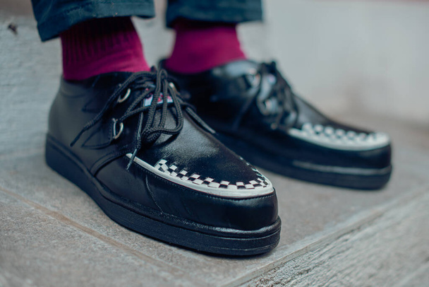 Young man sitting and wearing black genuine leather creepers sneakers. These casual yet elegant shoes are handmade by an at-home shoemaker, perfect for hanging out on a sunny day - Foto, Imagem